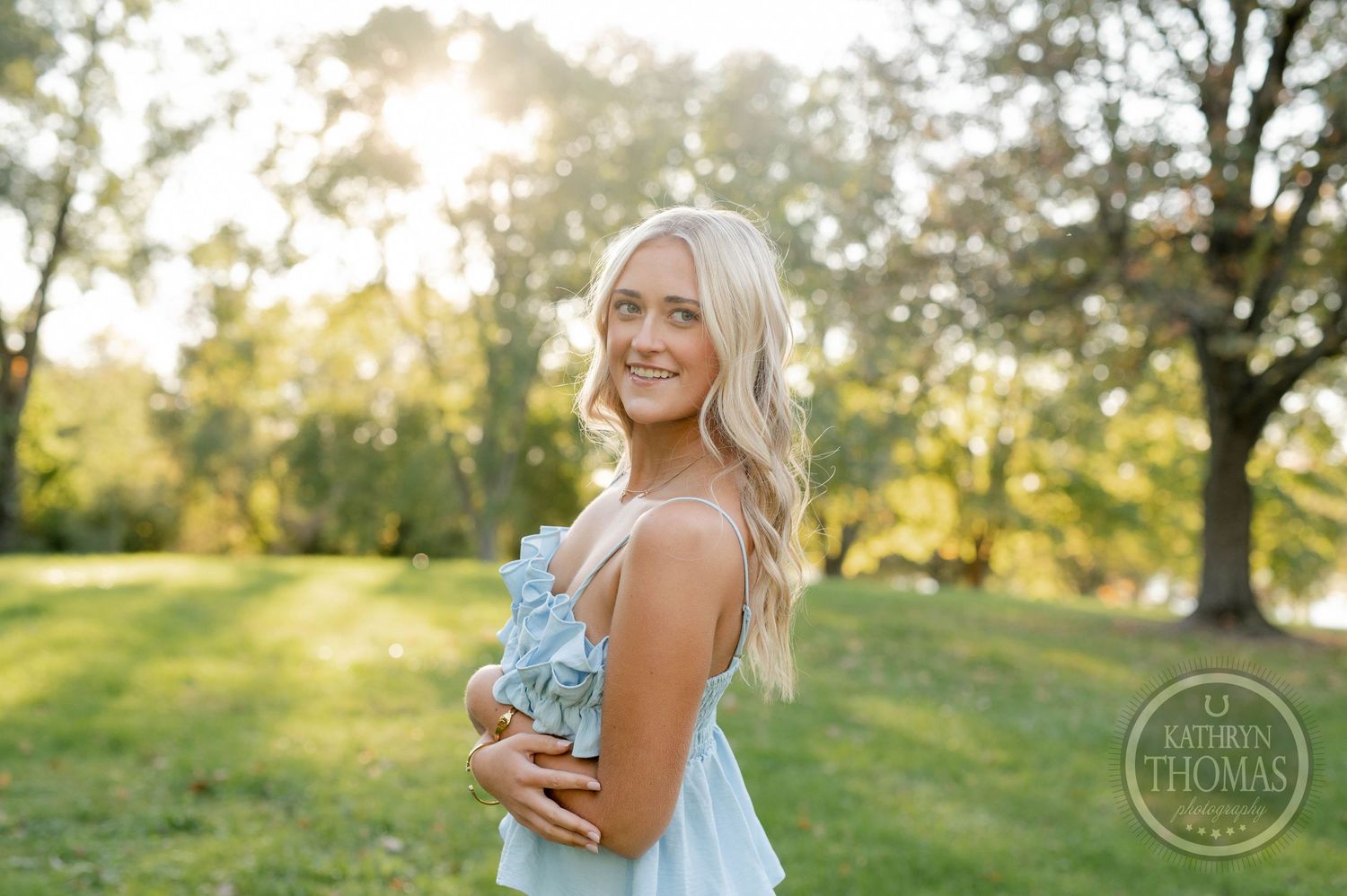 Person in light blue ruffle top poses in sunlit garden setting with golden hour lighting.