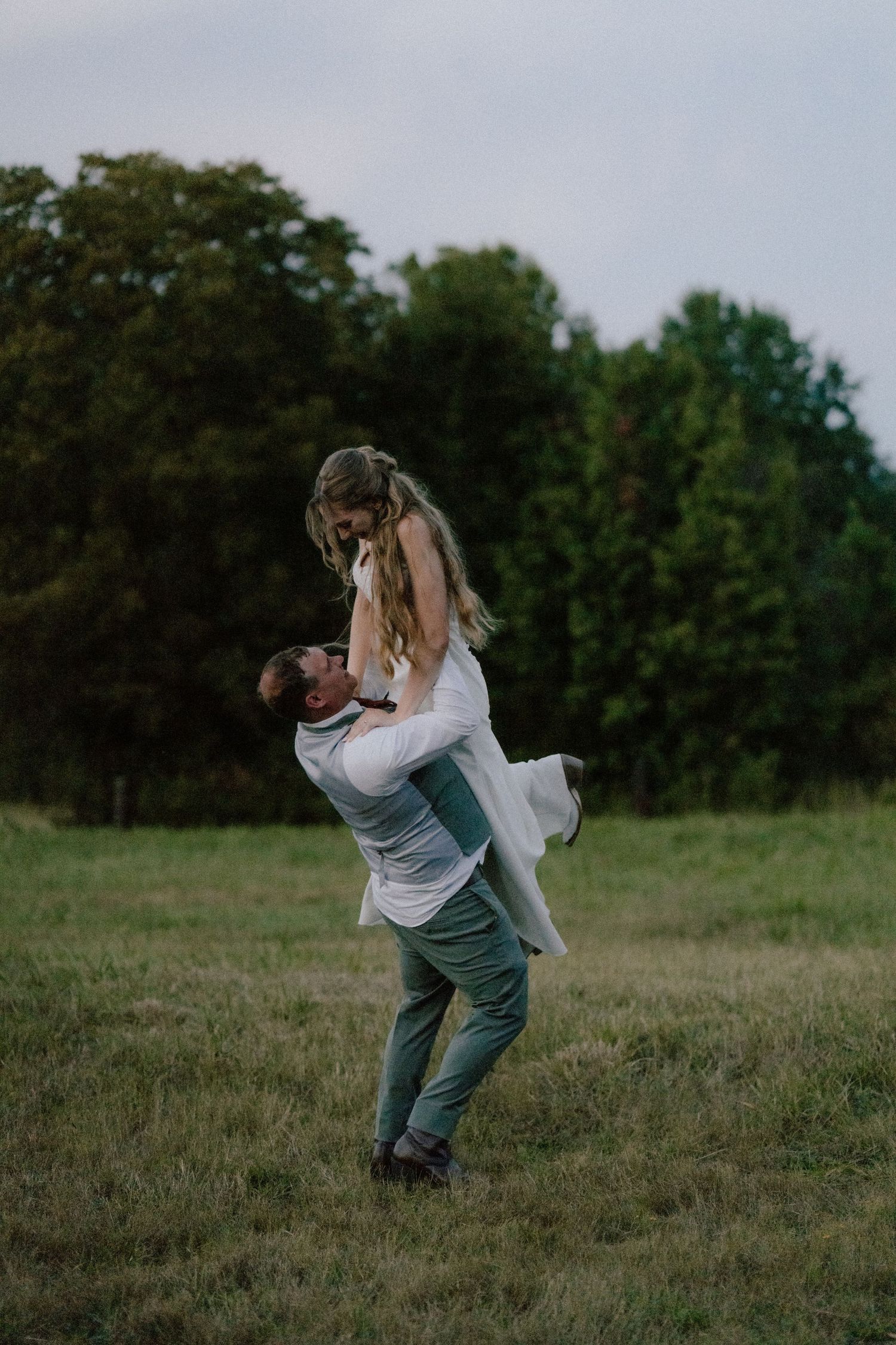 Romantic sequence of couple embracing and spinning in a grassy meadow at dusk.