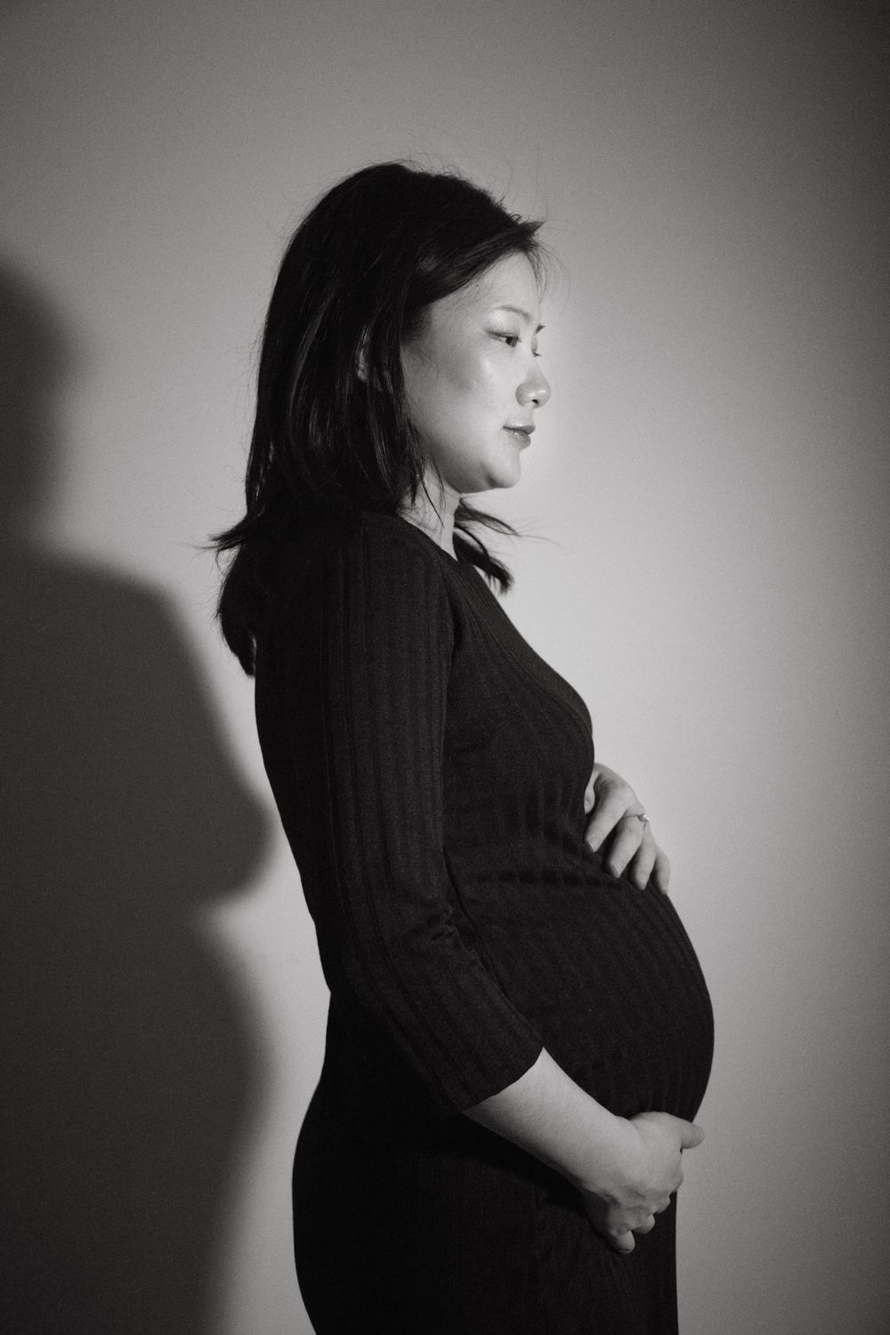 Black and white portrait of expectant mother in profile wearing dark clothing against light background.