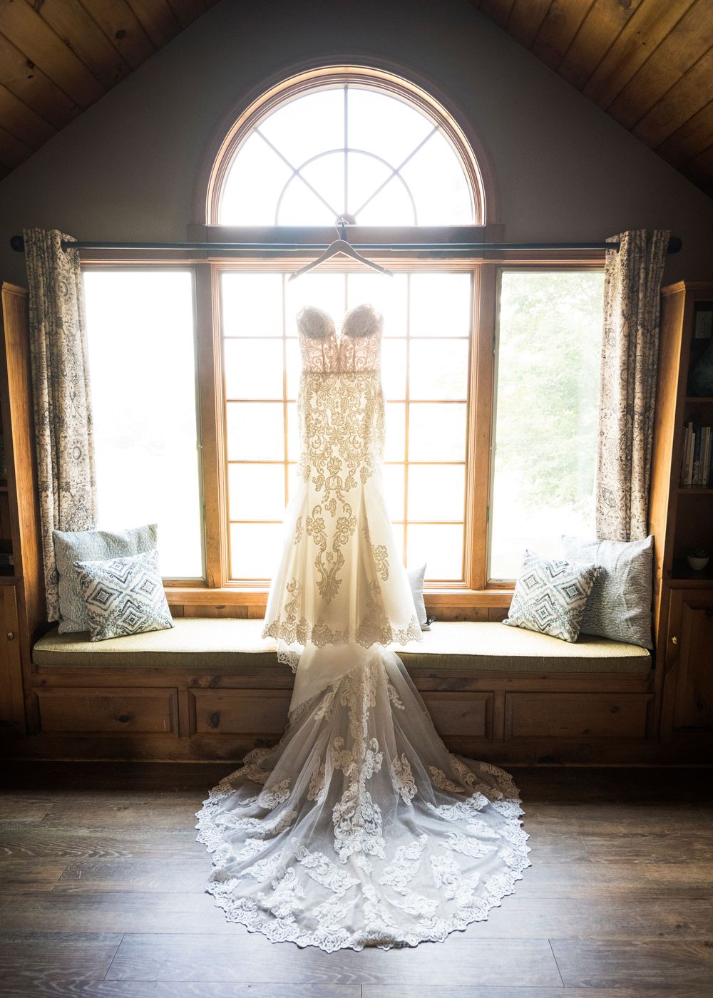A stunning lace wedding dress train displayed in sequence across rustic wood floors near large windows.