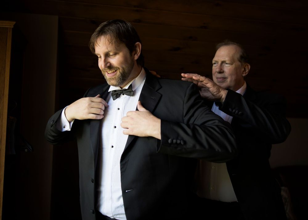 Two men in black tuxedos adjusting their formal attire in a dimly lit room.