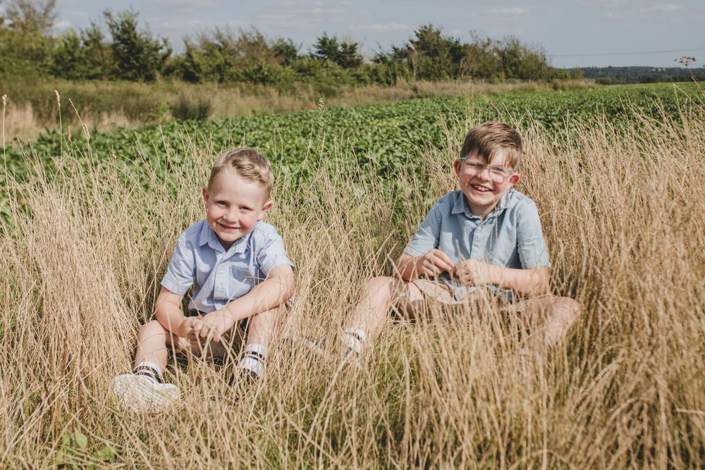 Two young boys sitting and smiling in tall grass on a sunny day.
Suffolk Family photos. Beckie Egan Photography.