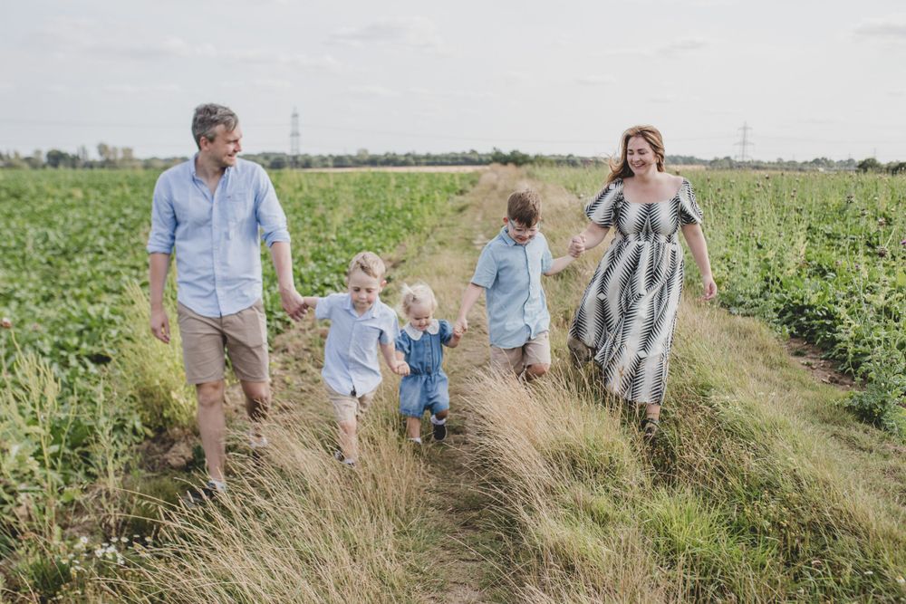 Family walking together along a rural path surrounded by green fields. 
Suffolk Family photos. Beckie Egan Photography.
