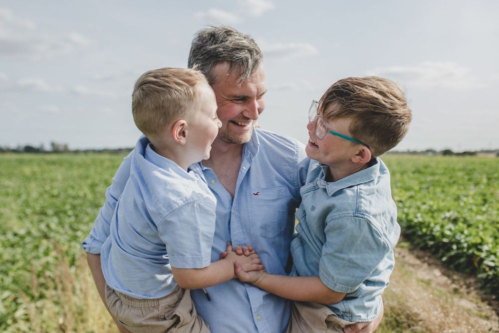 Joyful moment shared between parent and children in a sunny agricultural field. Suffolk family photos. Beckie Egan Photography.