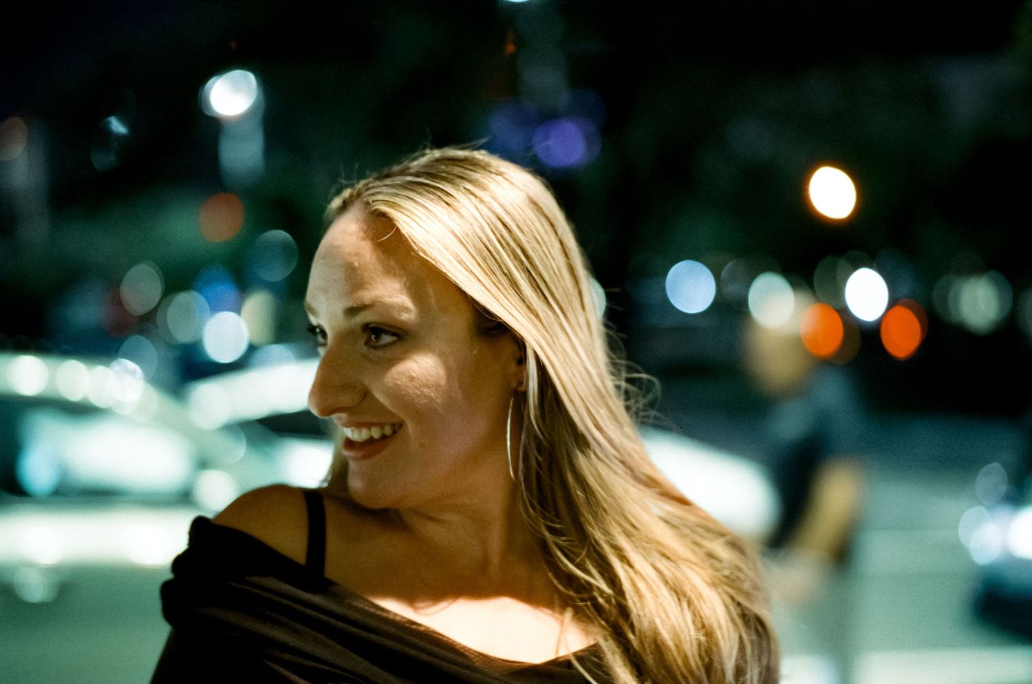 A candid nighttime portrait shows a delighted expression with city lights twinkling in the dark background.