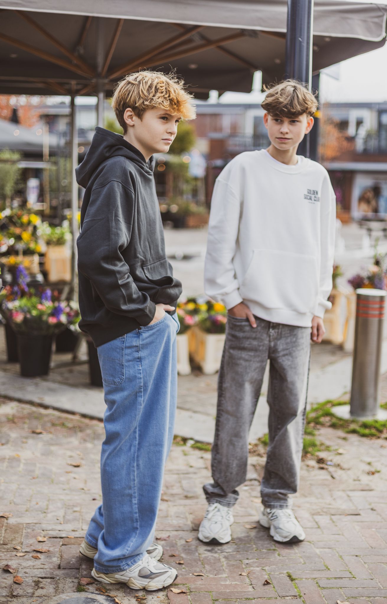 Person wearing grey tweed jacket holding dried flowers in front of floral display. campagneshoot kinderkleding collectie.