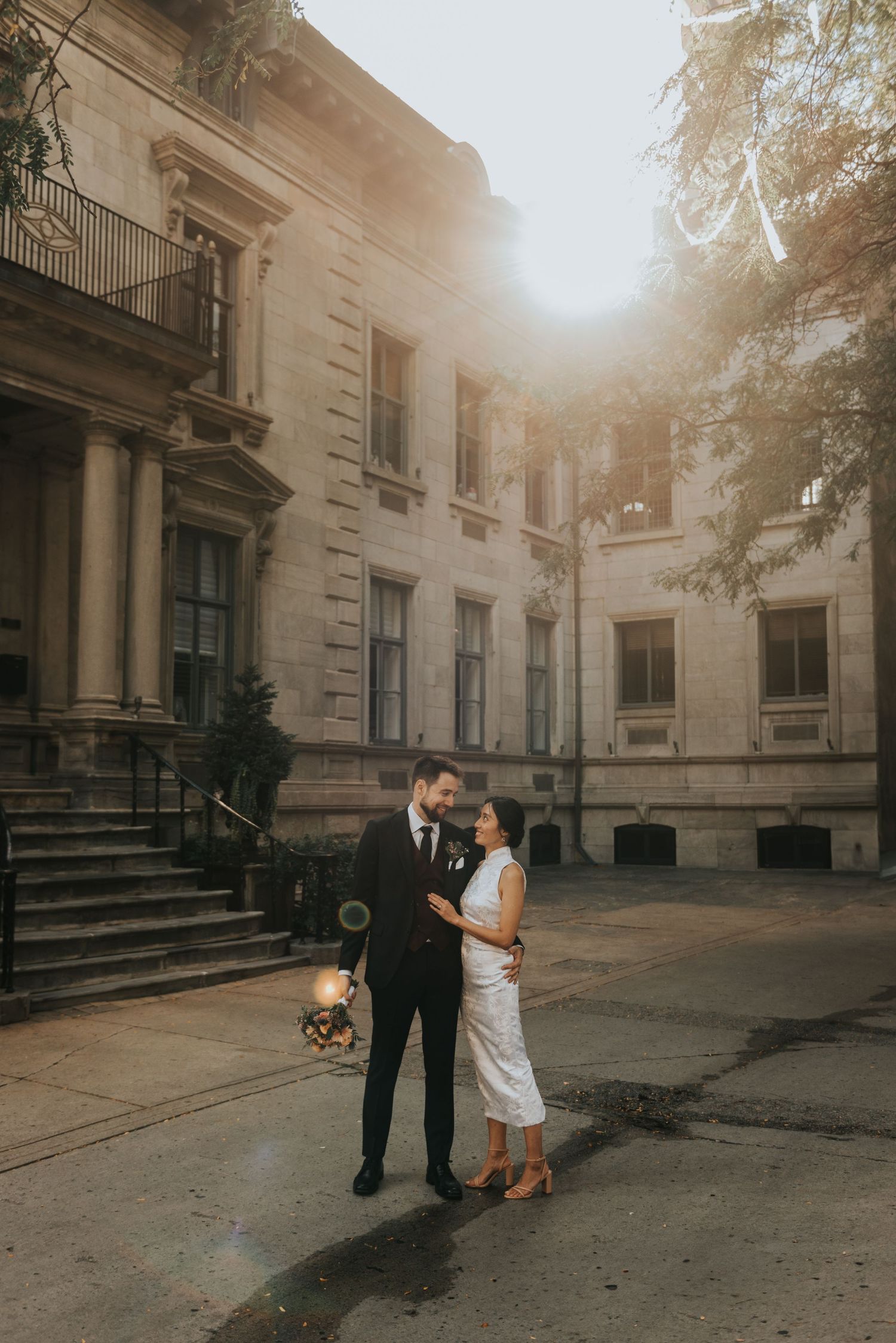 A romantic wedding couple embraces outside a grand historic building during golden hour.