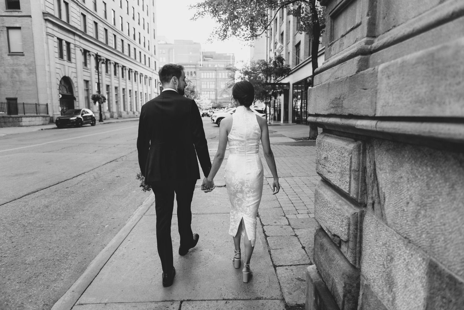 A couple walking together hand in hand down a city sidewalk in black and white.