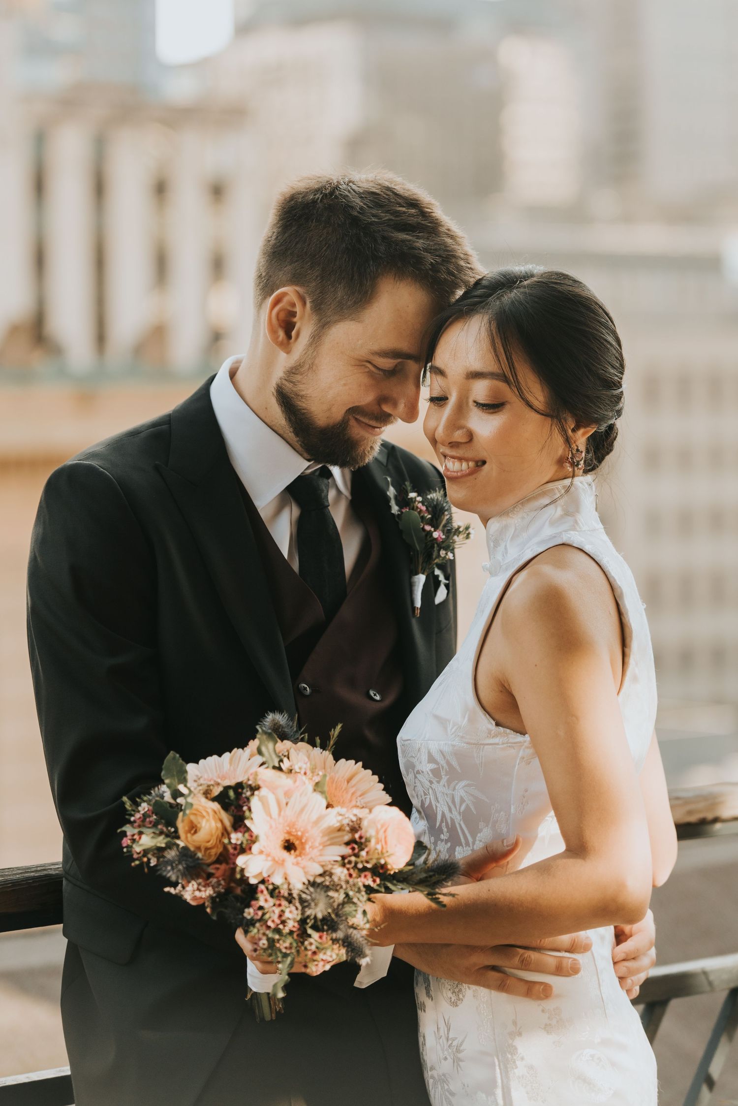 A romantic wedding couple sharing an intimate moment on a rooftop with a peachy pink floral bouquet.