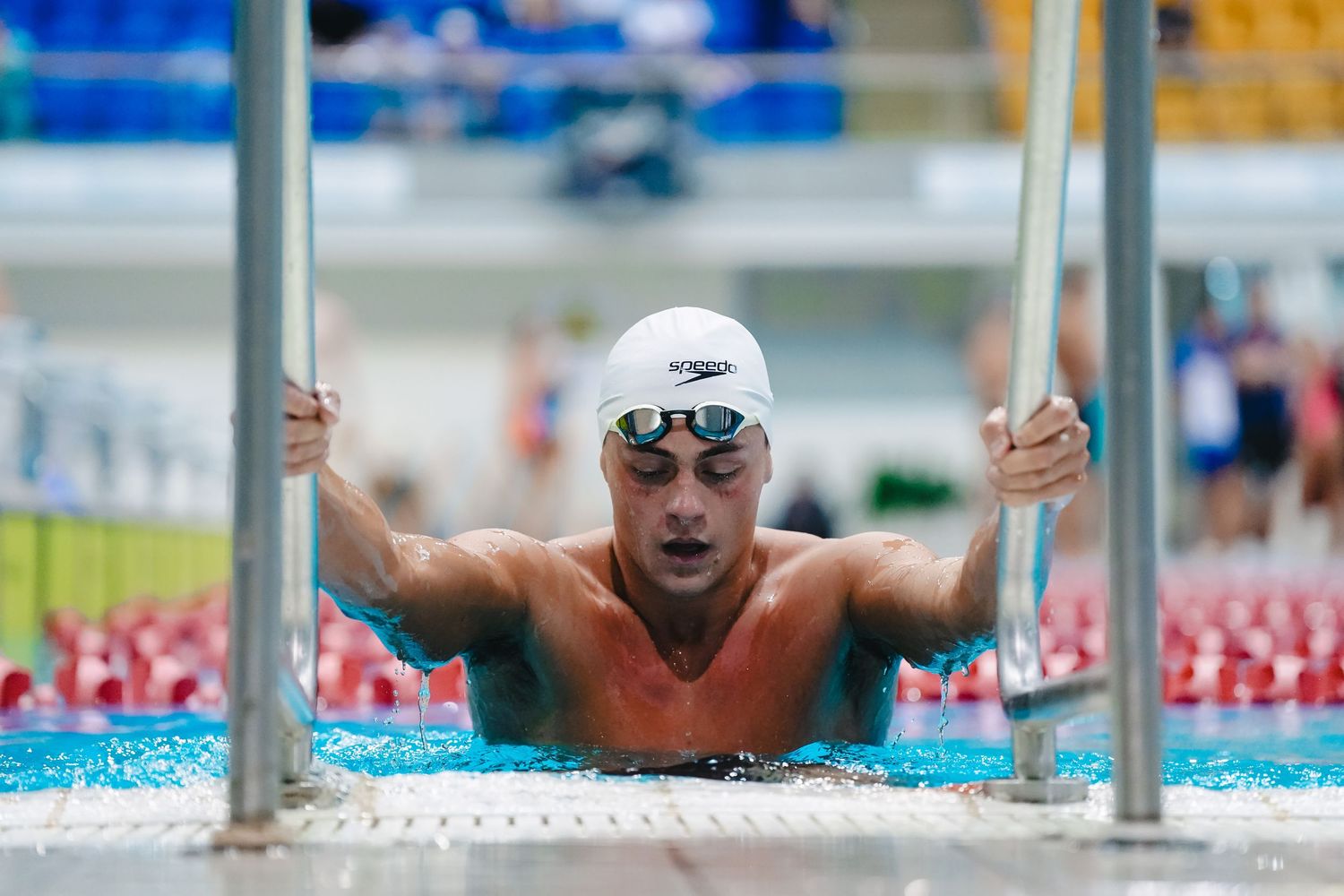 A swimmer emerges between lane markers during a competitive swimming race at an indoor pool.
