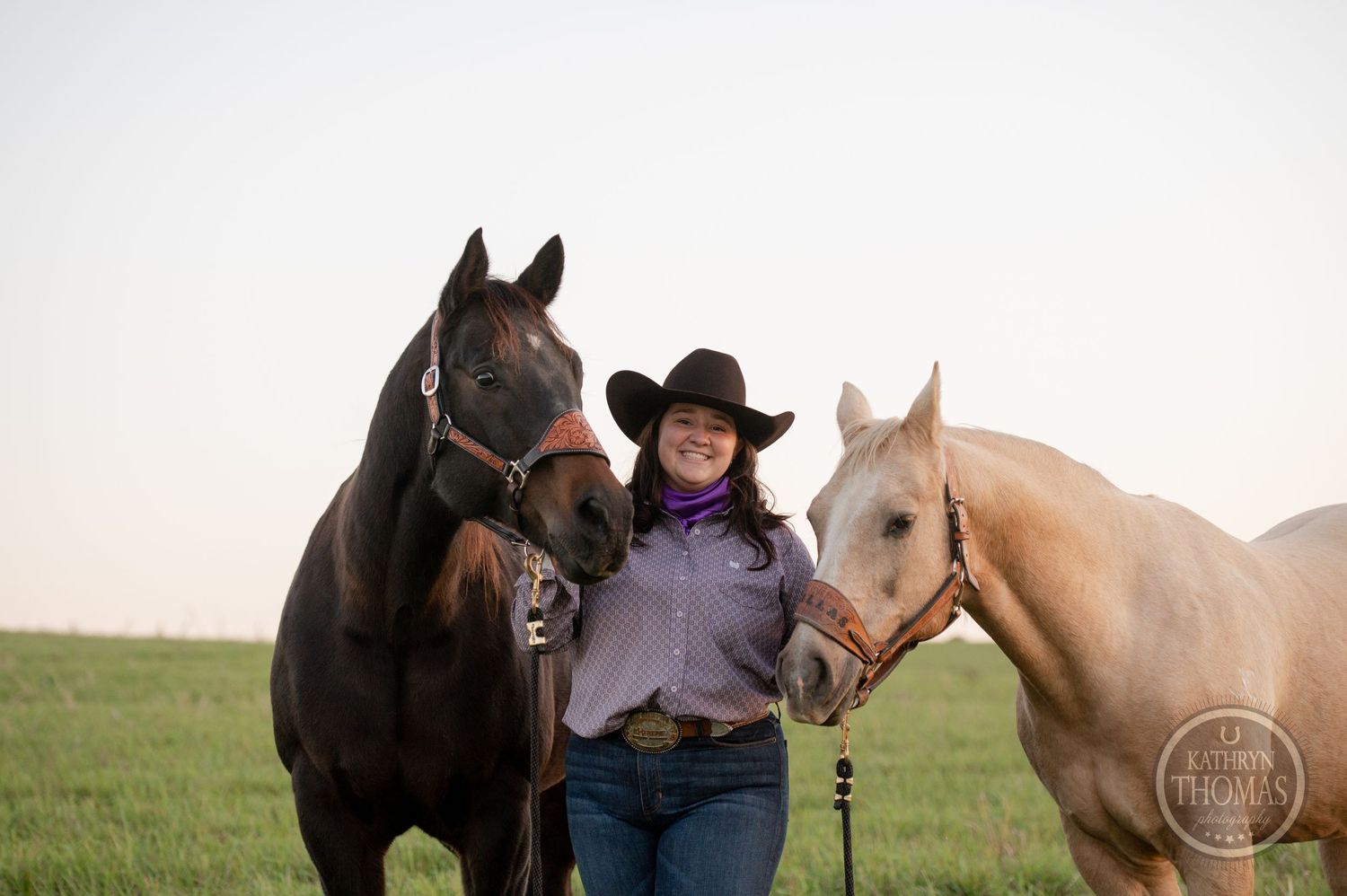 Two beautiful horses, one dark and one light, pose with their handler in a grassy field.