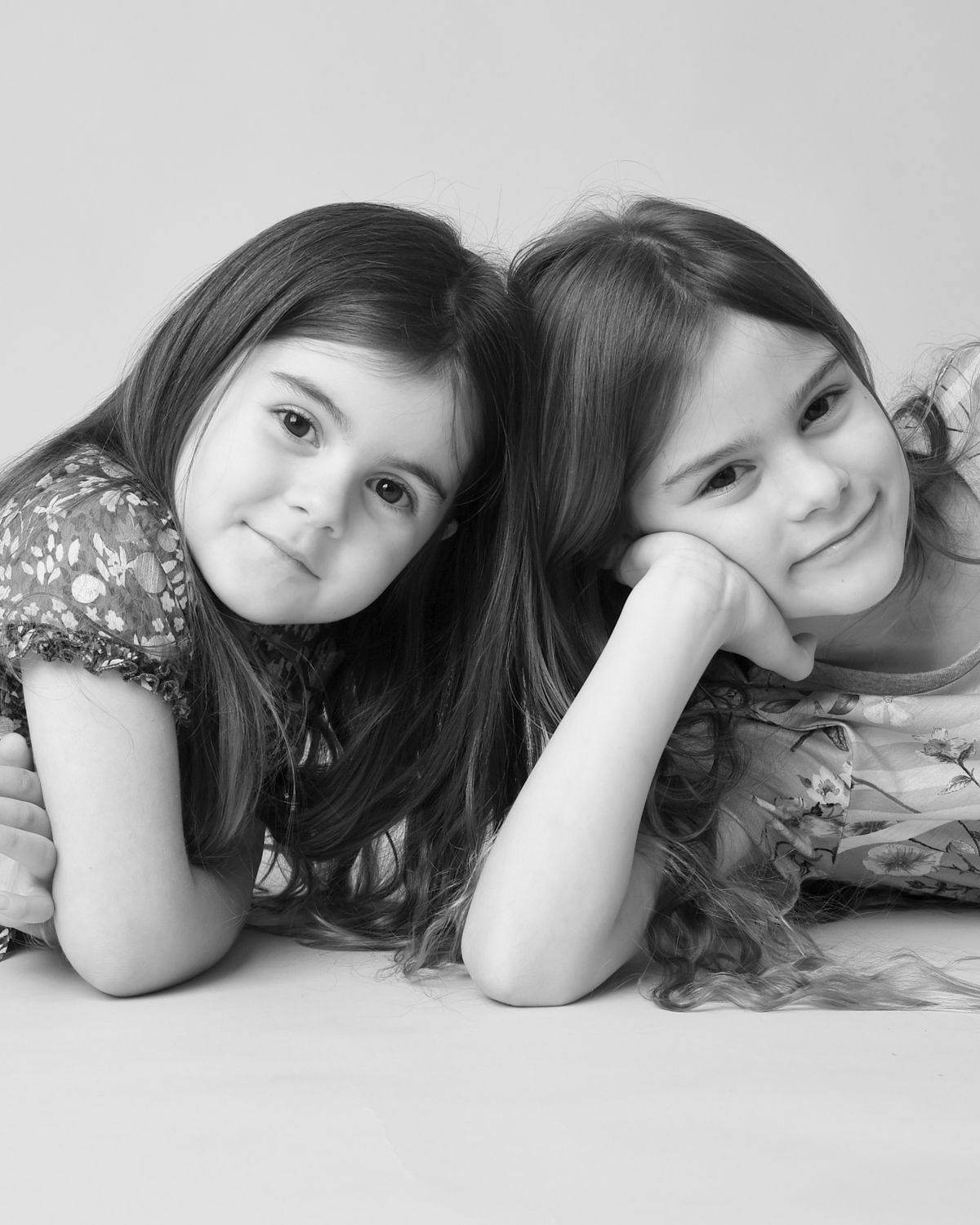 Black and white portrait of two young sisters lying on the floor, taken by Abigail's Studio in High Wycombe.