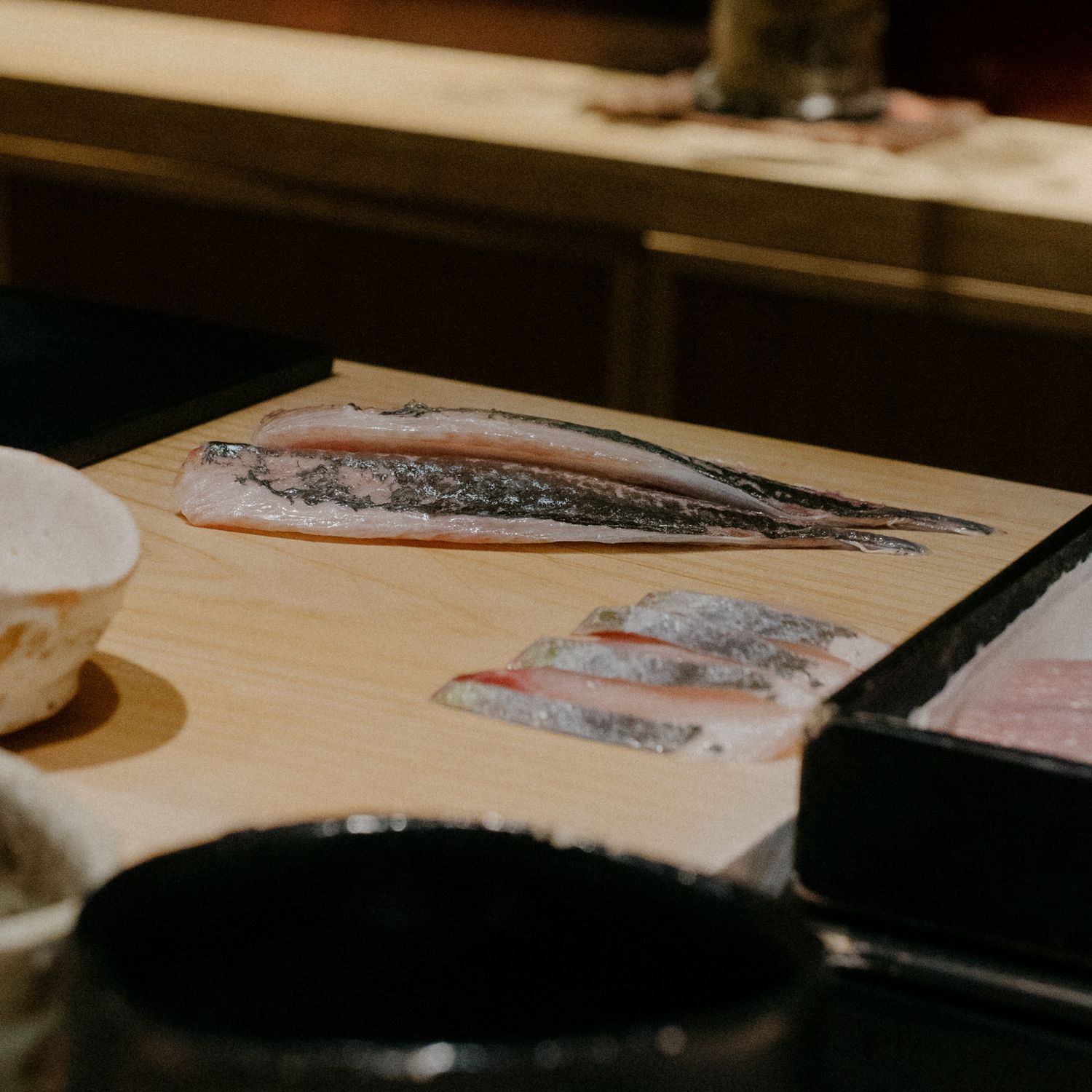 Fresh fish fillets being prepared on a wooden cutting board at a sushi counter.