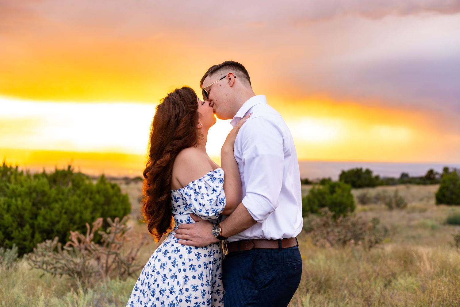 Romantic couple portrait against vibrant orange sunset sky in desert landscape.