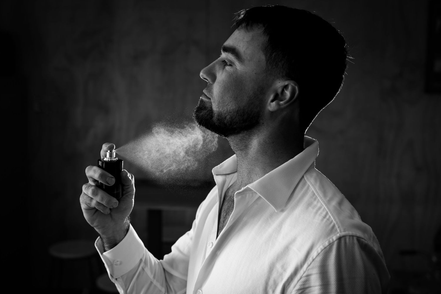 Dramatic black and white portrait of a man blowing smoke in dark lighting.