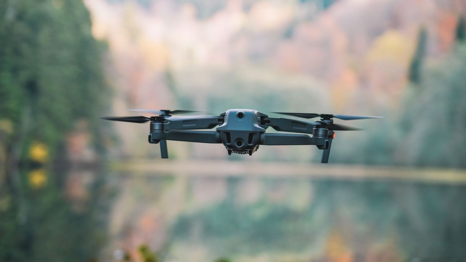 Drone flying in air against blurred autumn forest background.