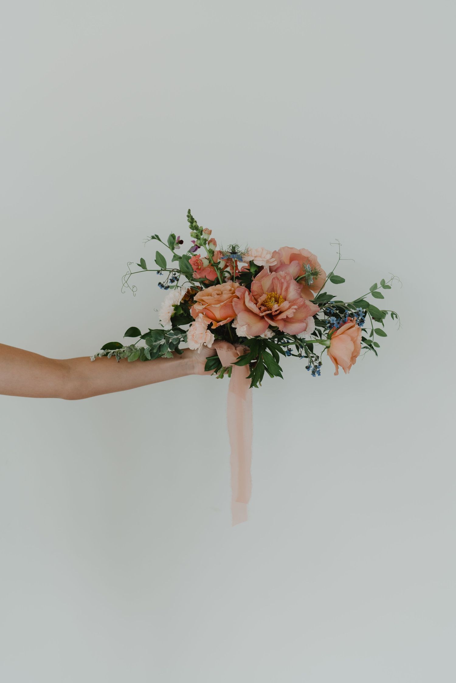 Delicate floral arrangement with peach roses and greenery held against a light gray background.