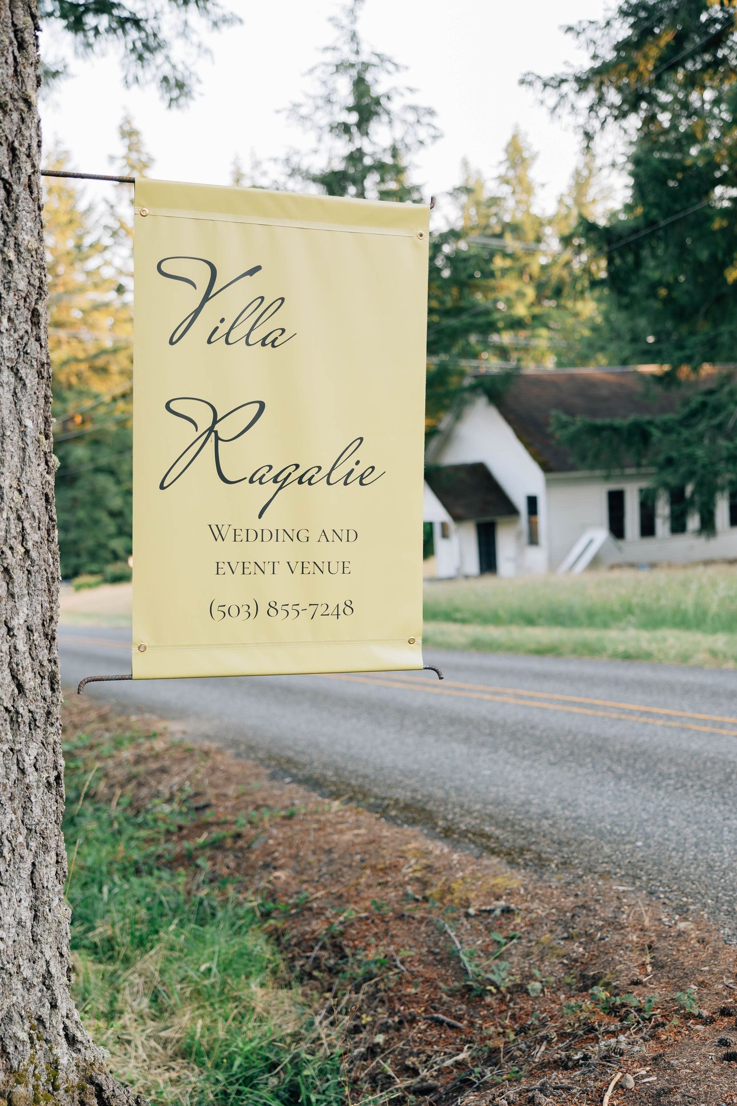 Yellow sign for Villa Ragalie wedding and event venue displayed on a tree by a rural road.