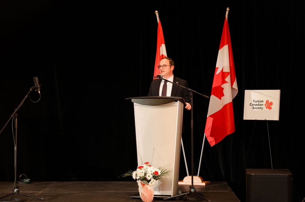 Speaker at podium with Canadian and Turkish flags during formal presentation.