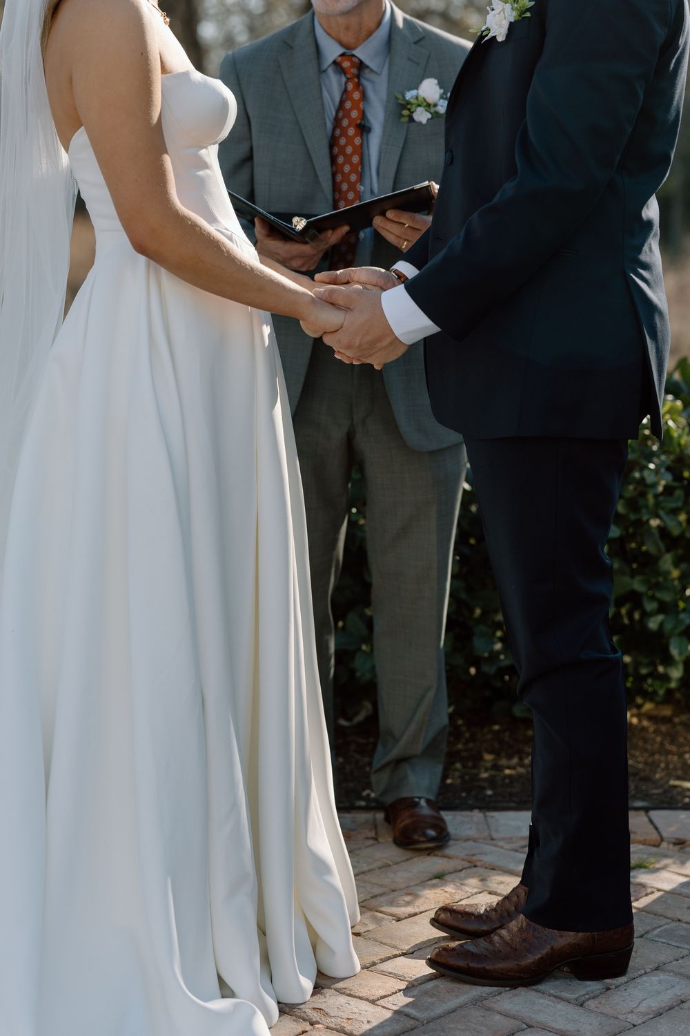 Wedding ceremony attendees stand on brick pavers during an outdoor garden ceremony.