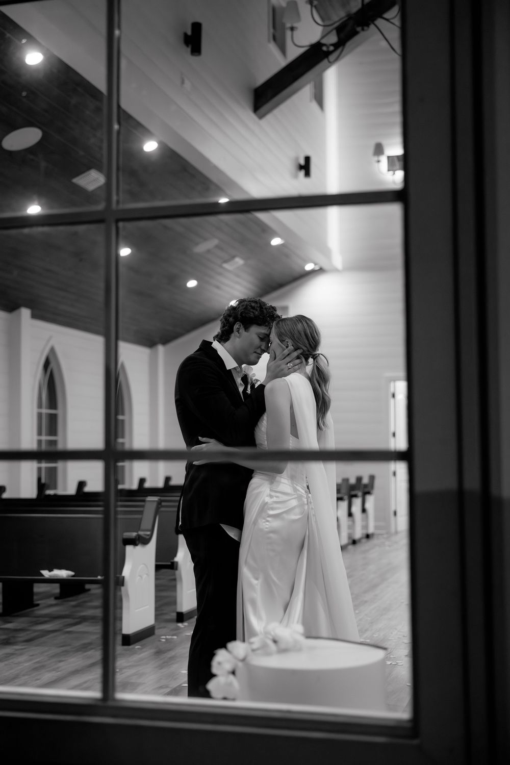 A romantic black and white wedding photo series showing a couple sharing intimate moments through church windows.