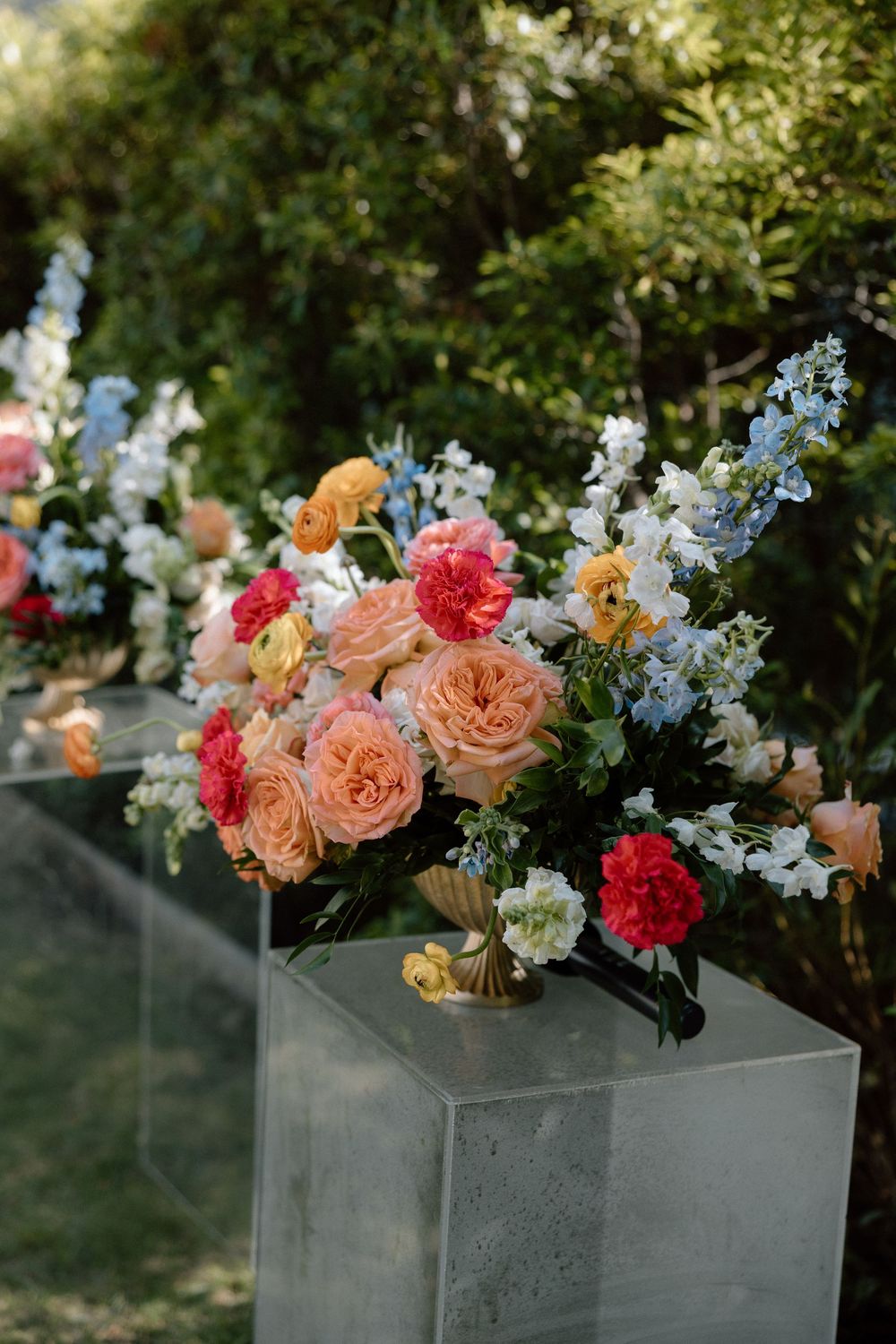 Colorful floral arrangement with pink, peach and white blooms in a modern concrete planter box against a garden backdrop.
