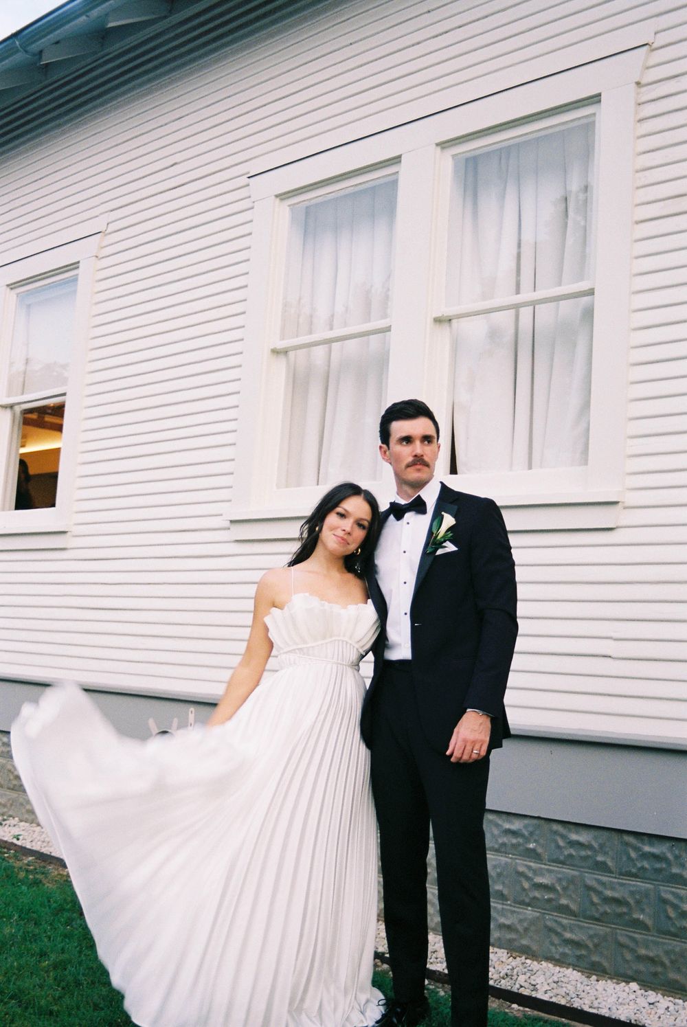 A couple in formal wedding attire poses together against a white building exterior in a series of candid shots.