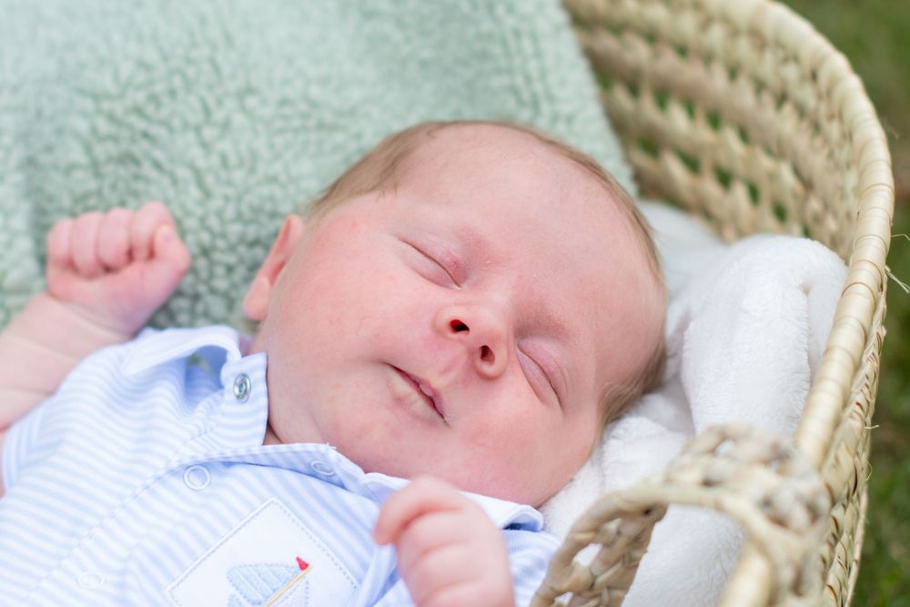 Sleeping newborn baby in blue outfit resting peacefully in wicker basket.