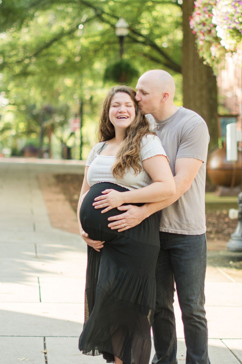 A joyful maternity photo of an expecting couple sharing a tender moment outdoors on a sunny day.