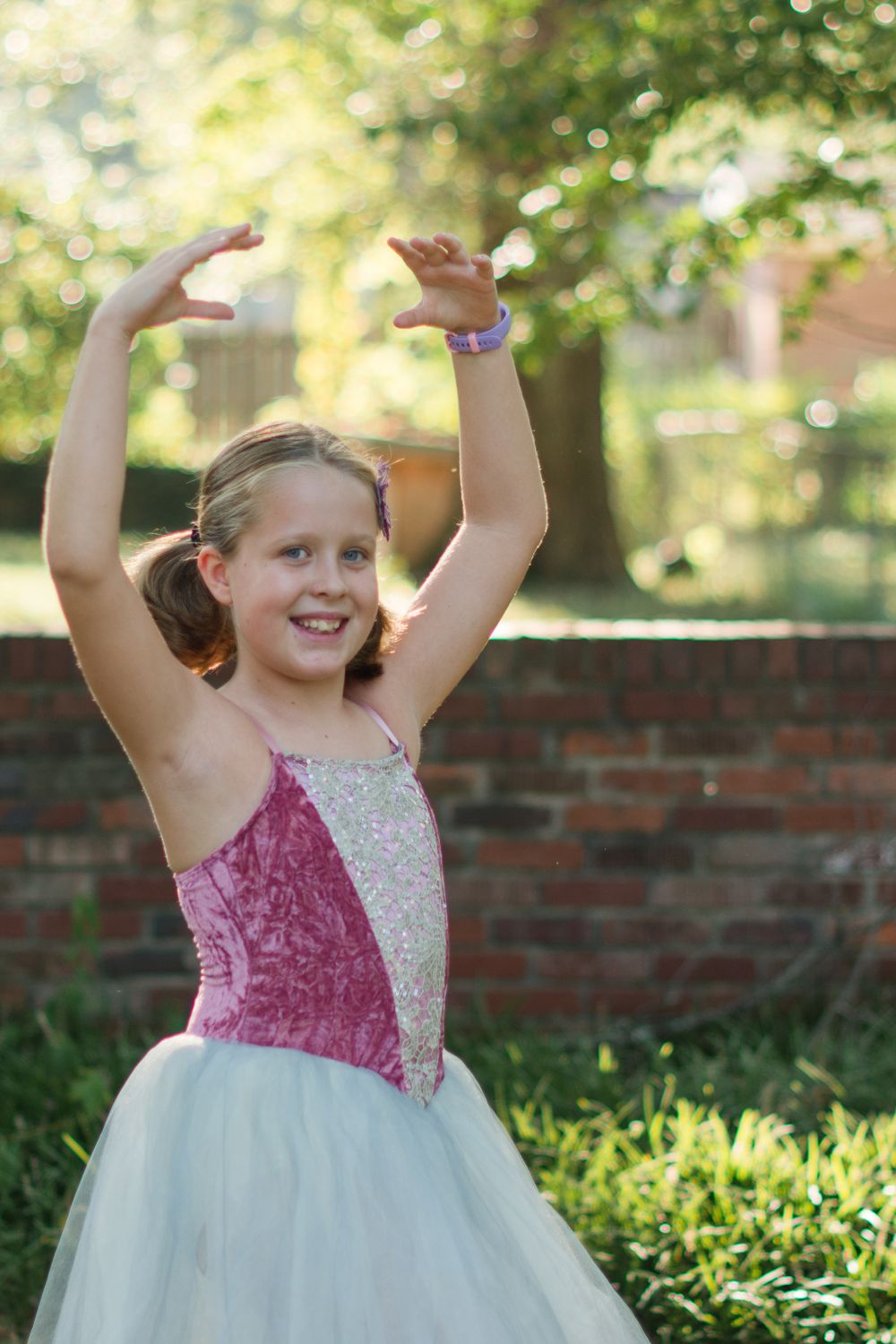 Young dancer in pink and white tulle dress poses gracefully in garden setting.