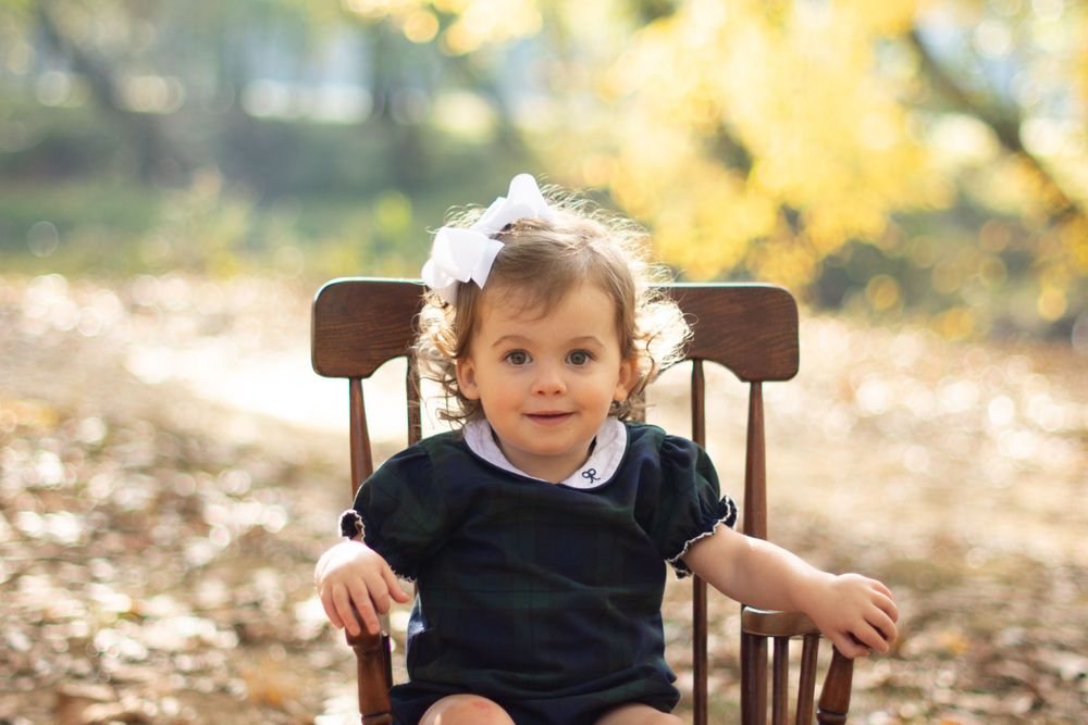 A small child sitting in a wooden chair outdoors during autumn.