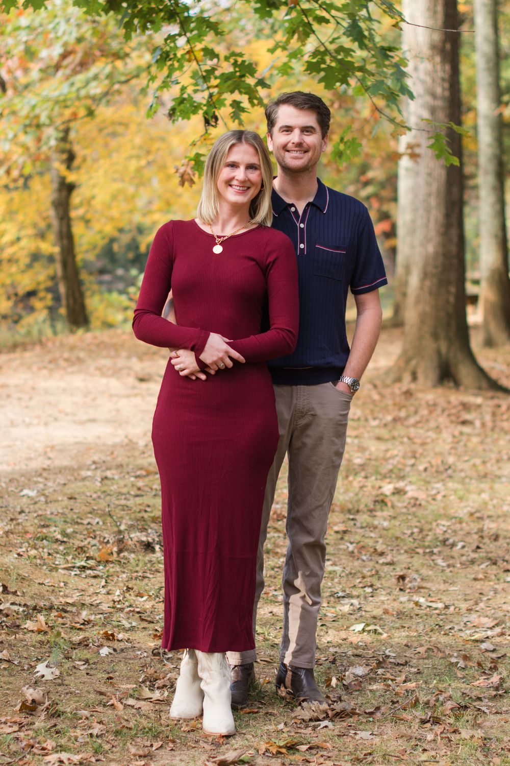 Couple posing on autumn trail with woman in burgundy dress and boots.