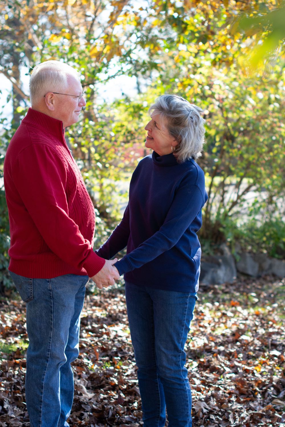 Loving senior couple holding hands surrounded by autumn foliage in a park setting.