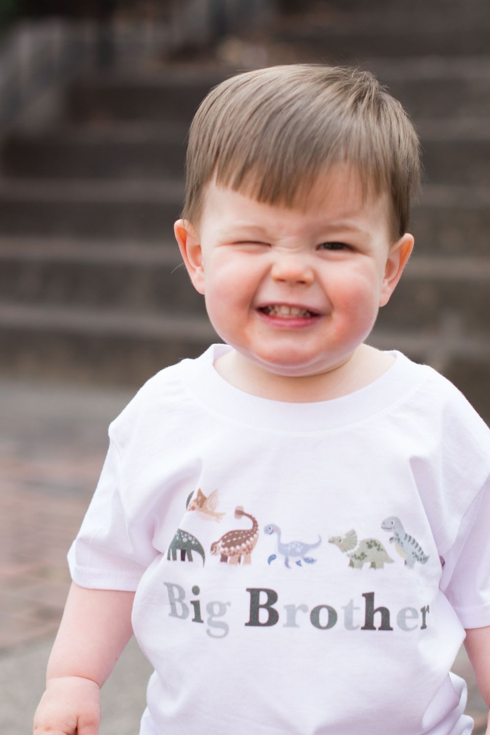 Toddler wearing a dinosaur-themed Big Brother shirt smiling joyfully.