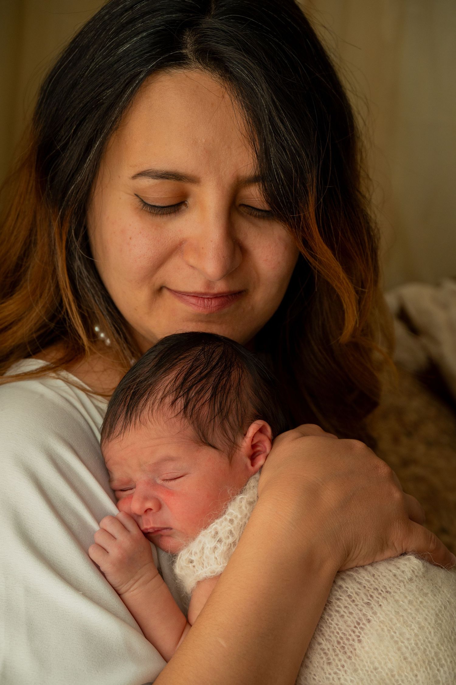 Intimate moment between parent and sleeping newborn baby wrapped in white clothing.