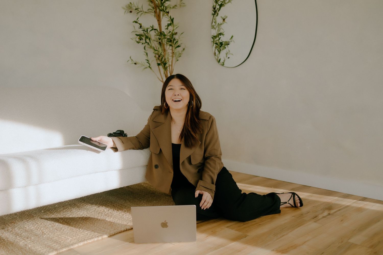 Person working on laptop while sitting on floor with plants in minimalist white room.