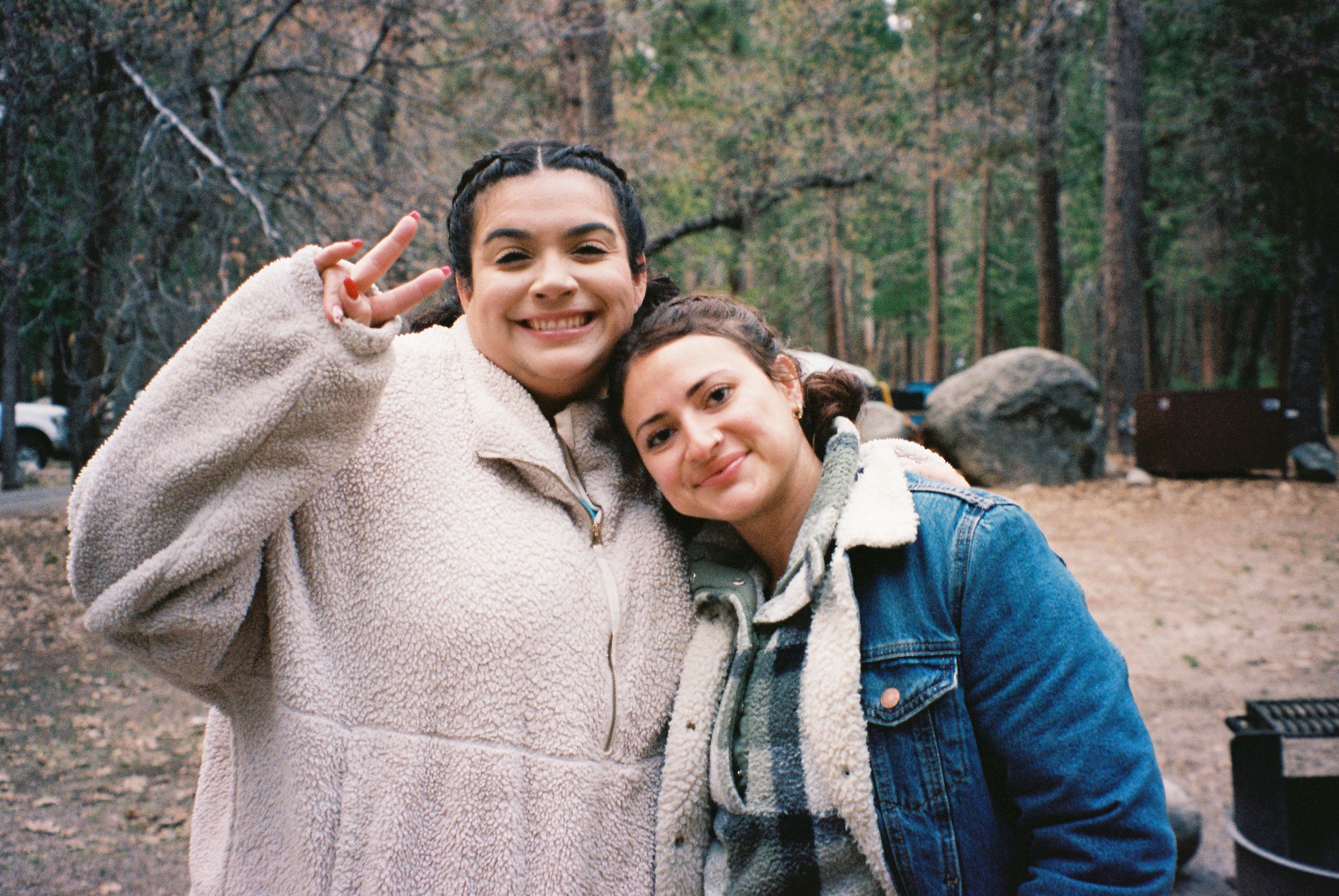 Two friends embracing outdoors in winter clothing with trees in the background.