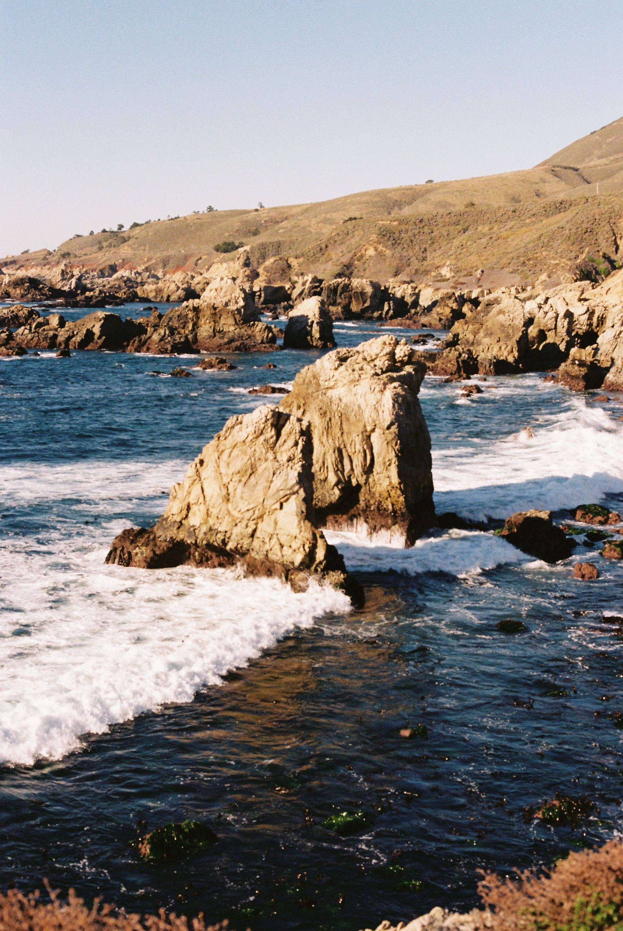 Rocky coastline with jagged formations and crashing waves against golden cliffs.
