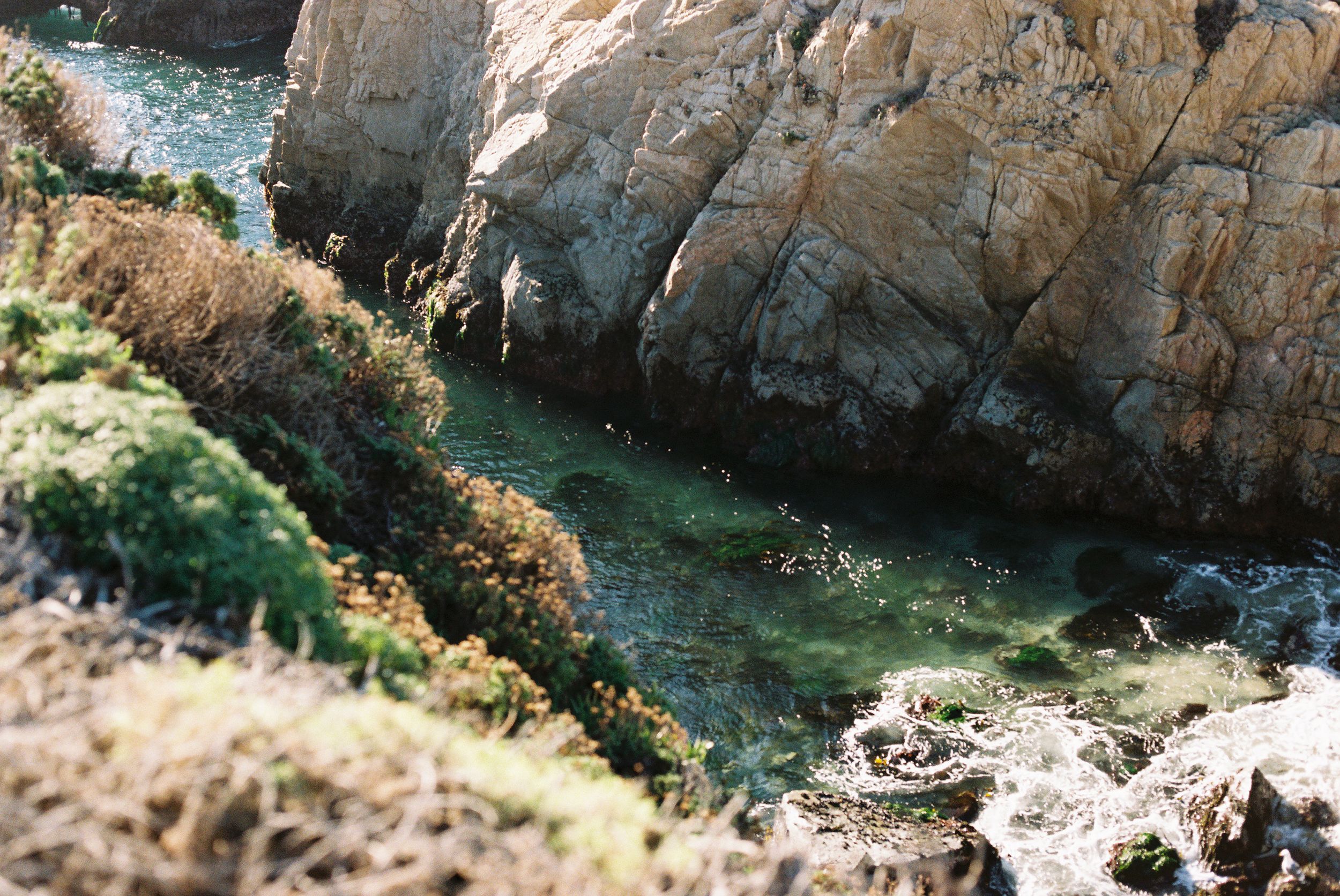 Rocky coastal cove with turquoise water surrounded by steep cliffs.