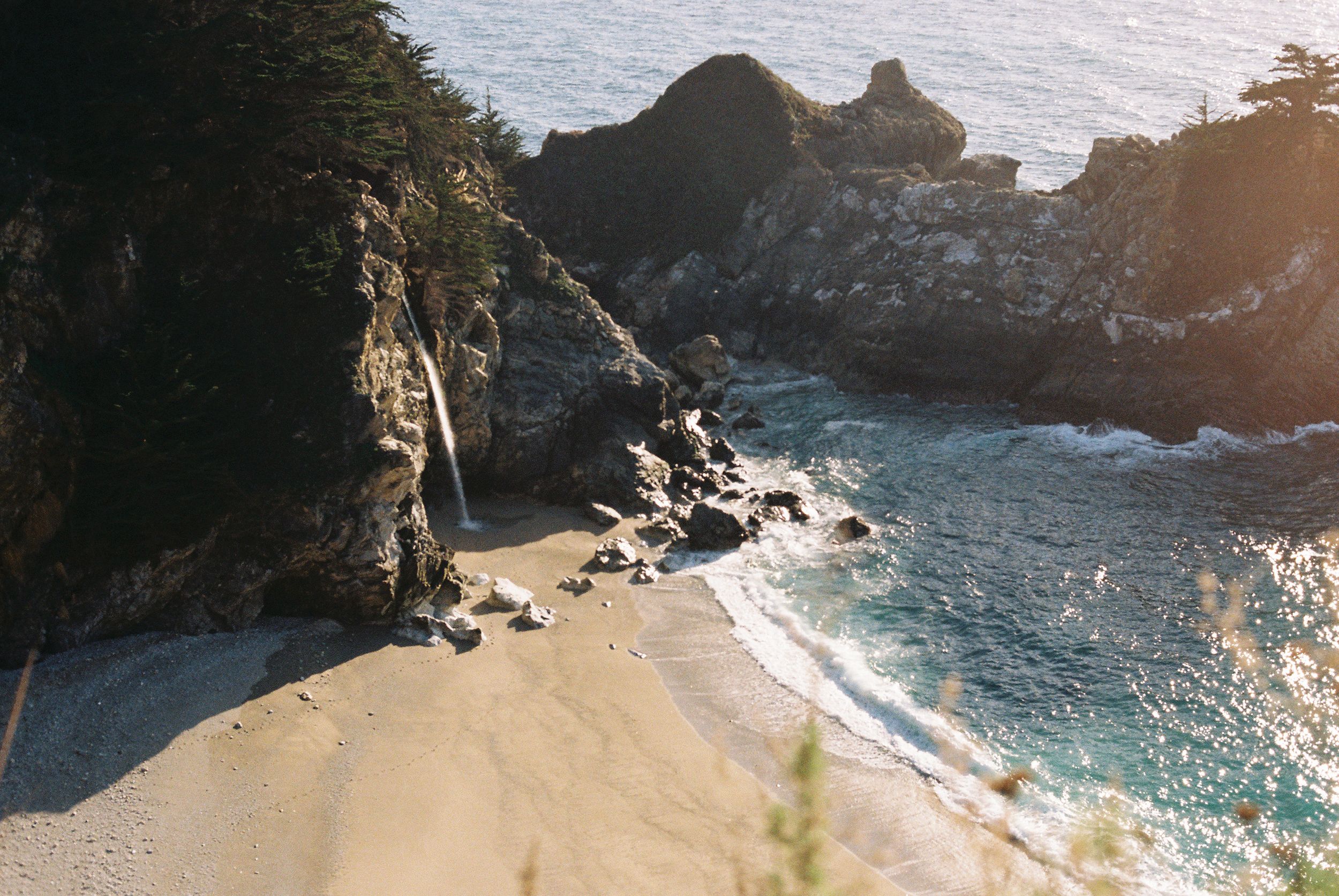 Secluded beach cove with turquoise waters surrounded by dramatic rocky cliffs at sunset.