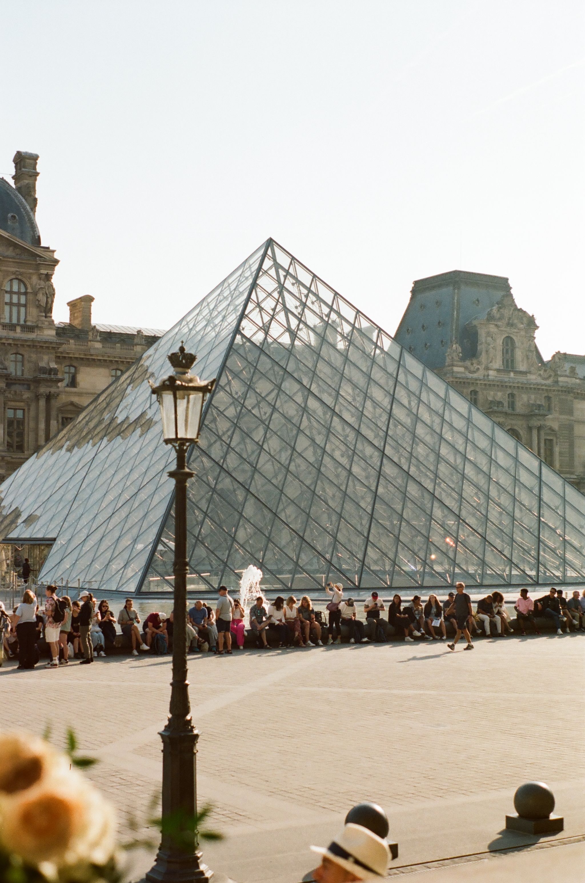 The glass pyramid entrance of the Louvre Museum with crowds gathered outside.