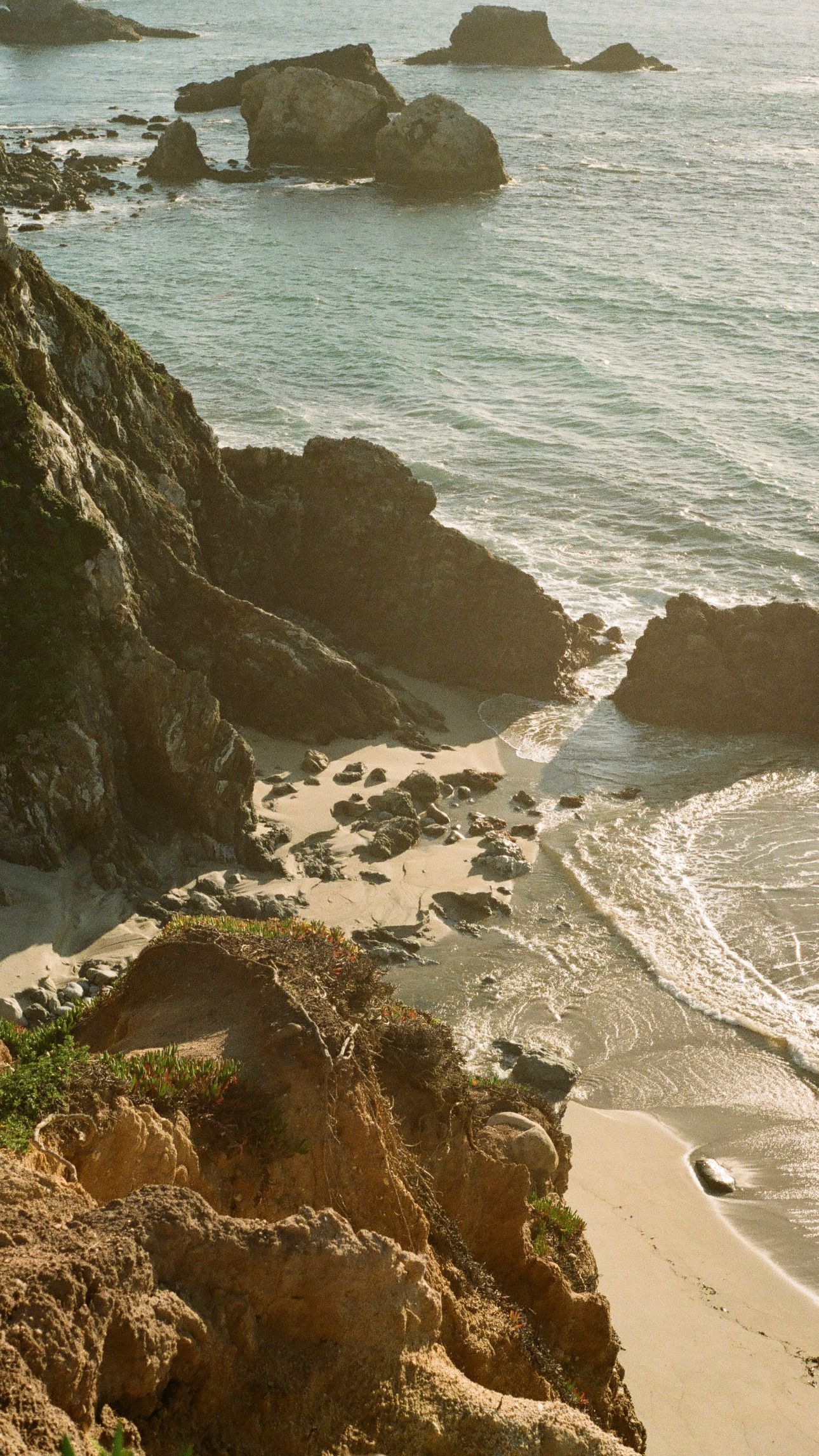 Rocky coastal cliffs meet turquoise waters at a secluded beach cove during sunset.