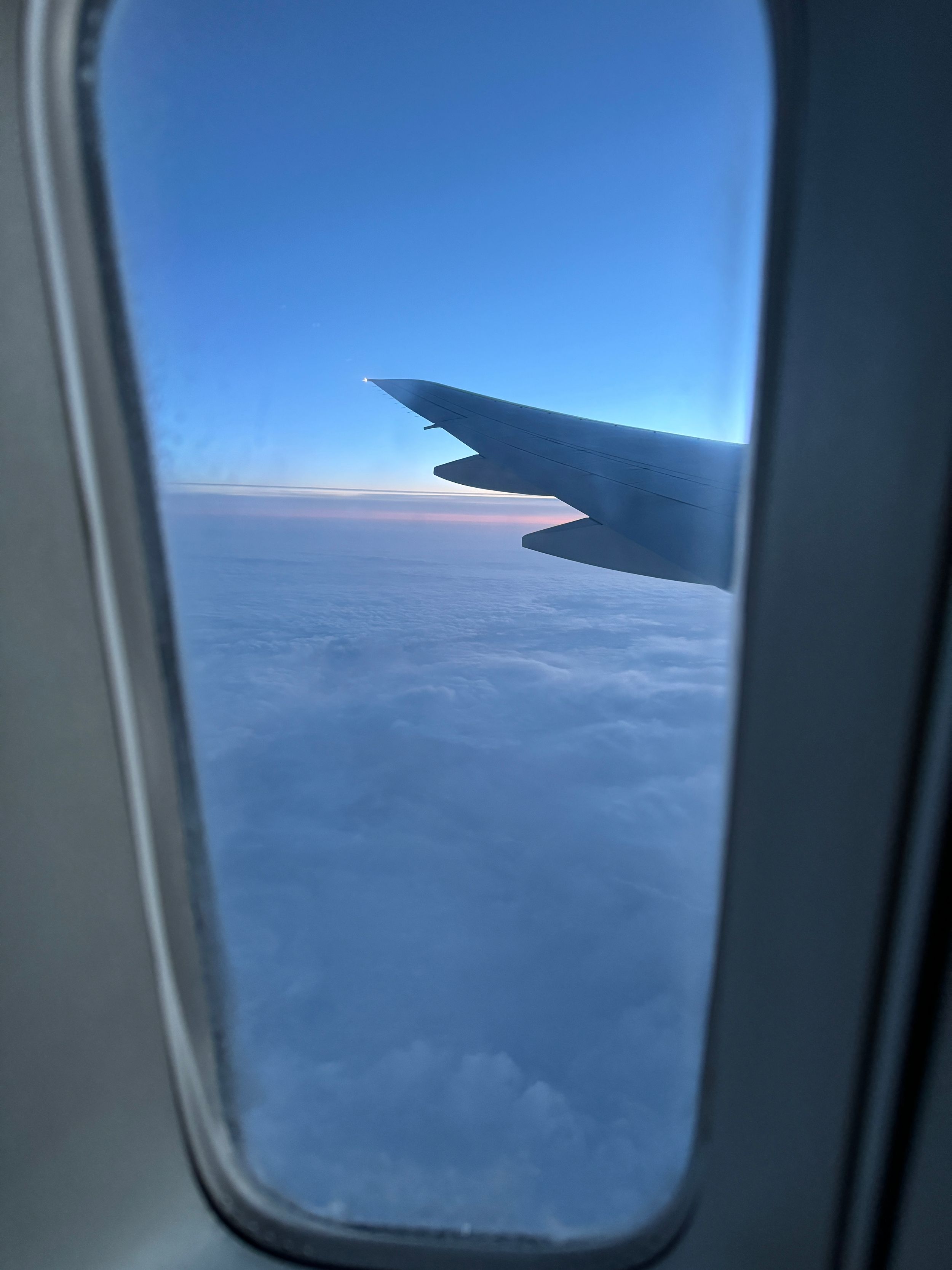 View of airplane wing against bright blue sky and clouds from passenger window.