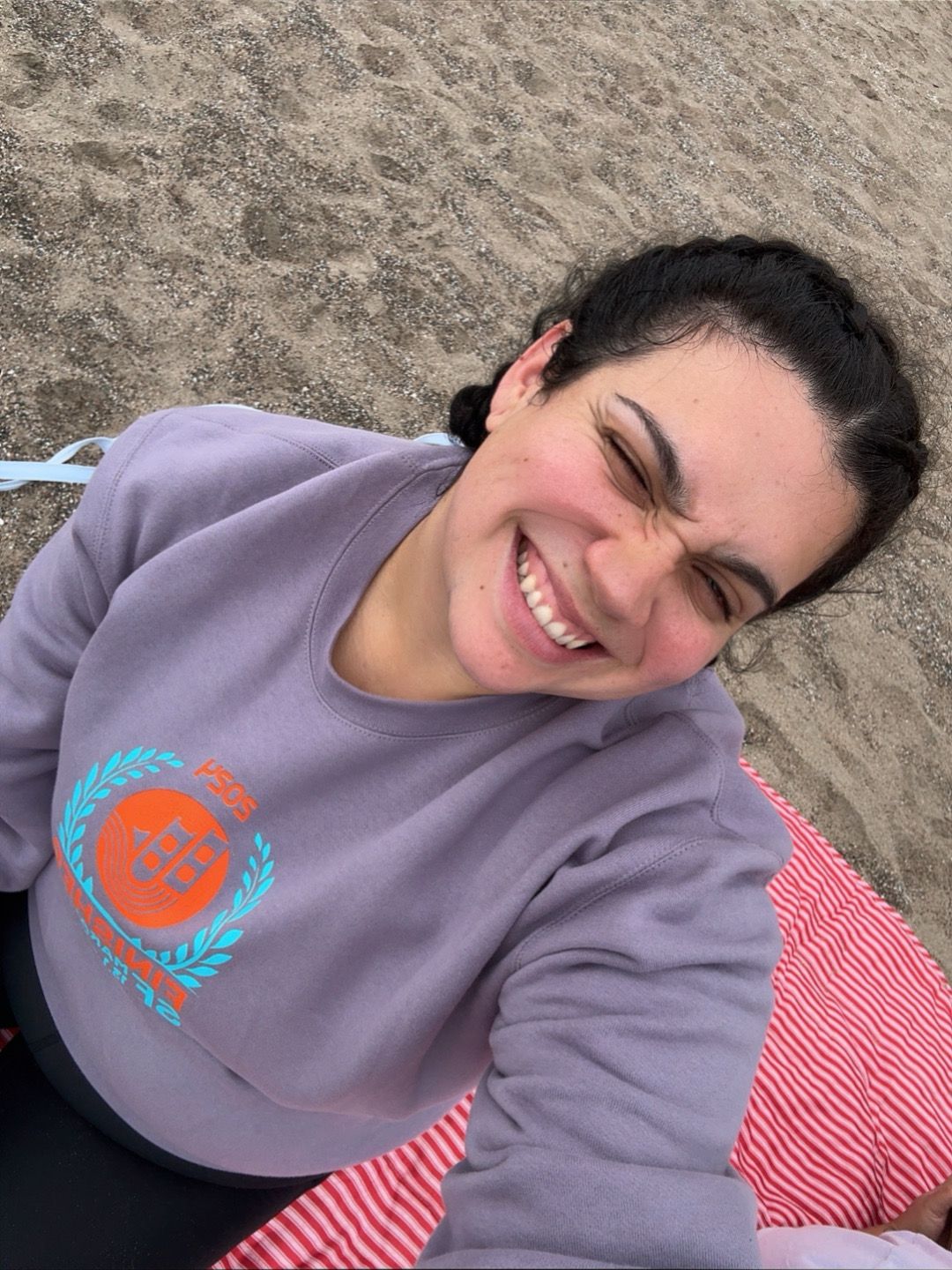 A person wearing a purple sweatshirt smiles while relaxing outdoors.