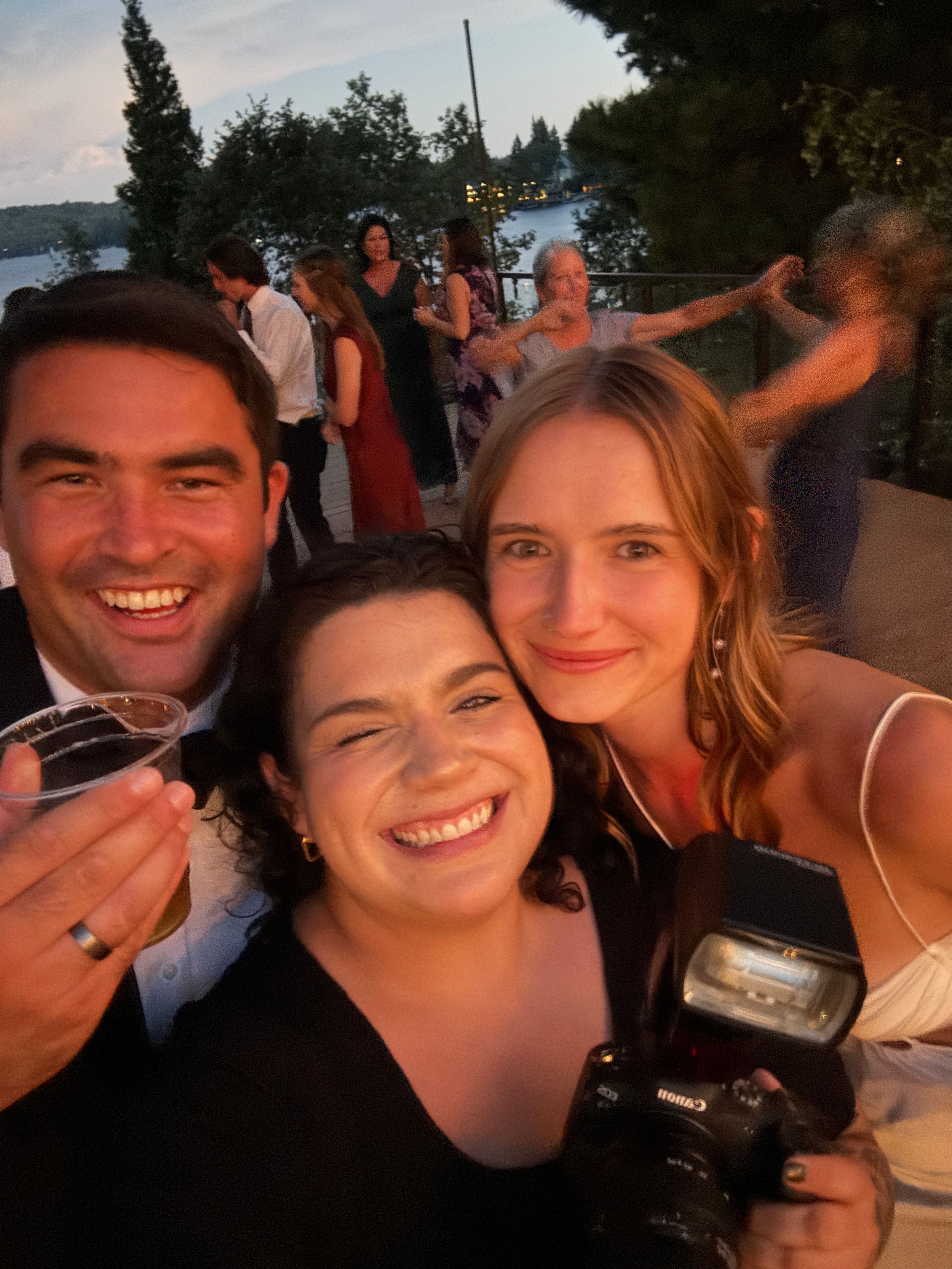 A group of photographers smile and pose together at an outdoor evening event.