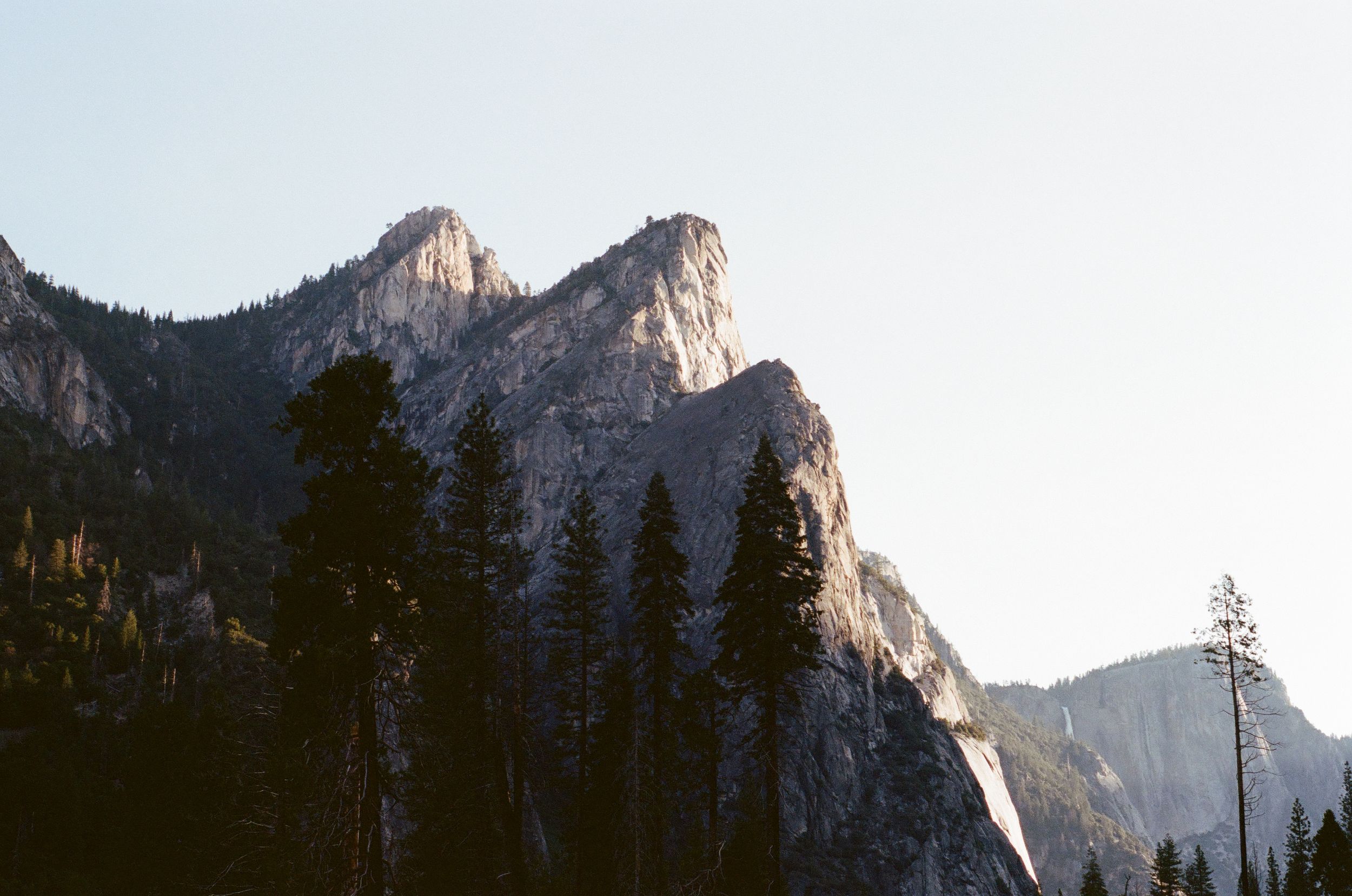 Dramatic granite peaks and evergreen trees create a majestic mountain landscape view at sunset.