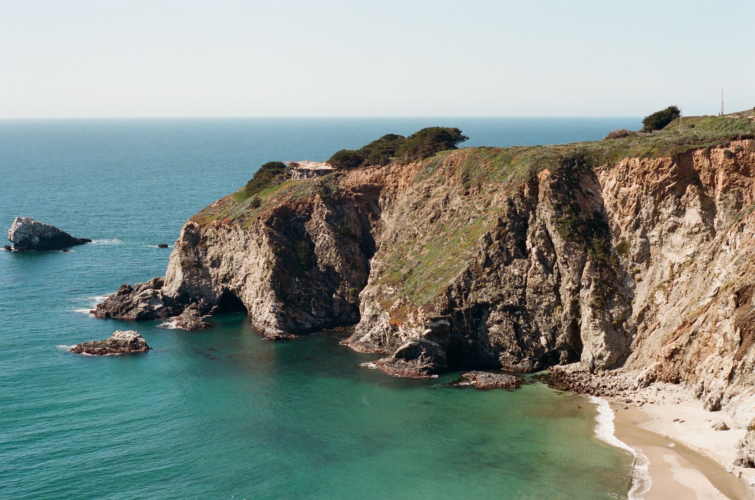 Dramatic coastal cliffs frame a pristine beach cove with turquoise waters.