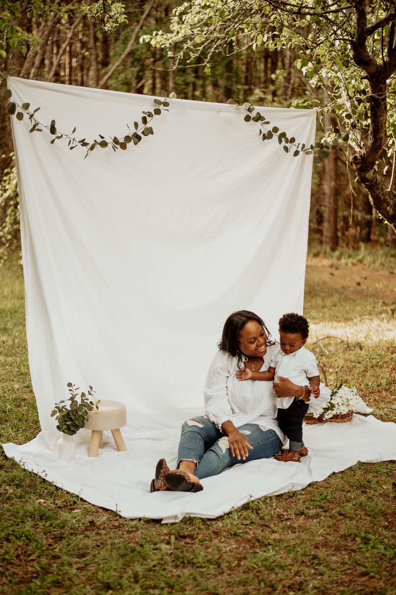 A cozy family photoshoot on a white blanket outdoors surrounded by trees and natural light.