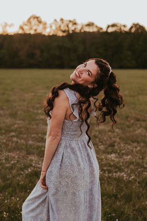 Person in grey dress twirls joyfully in field during golden hour photoshoot.