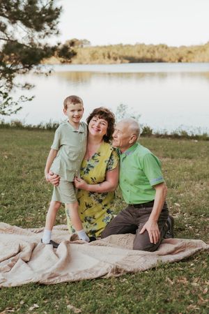 Family enjoys quality time together on blanket by lakeside during sunset photo session.